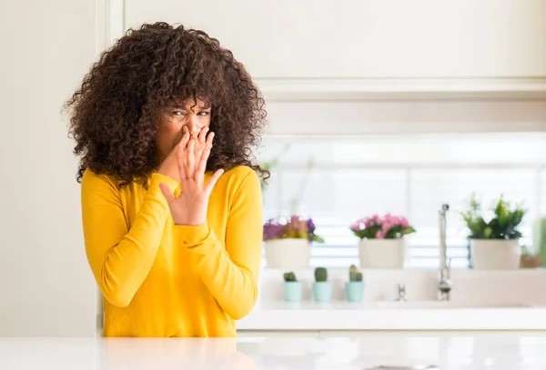 African American woman in kitchen smelling something disgusting
